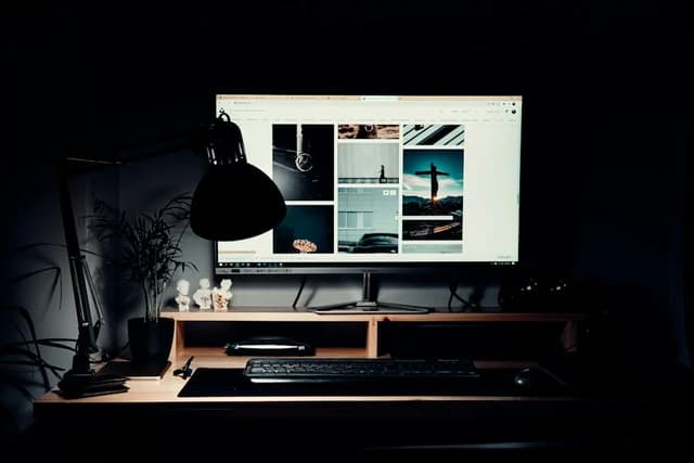 A monitor, keyboard and desk lamp in a softly lit workspace; editorial photograph, not a recommended model.